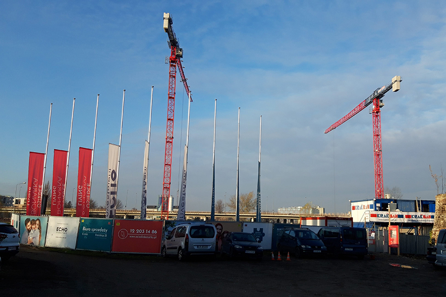 aquaberg.pl, panorama placu budowy na któym widać dzwigi żurawie oraz flagi z logami firm, m.in. firmy aquaberg
                            
                            